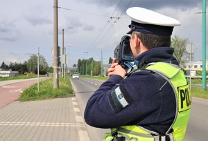 Policjant ruchu drogowego sprawdzający prędkość kierujących laserowym miernikiem prędkości.